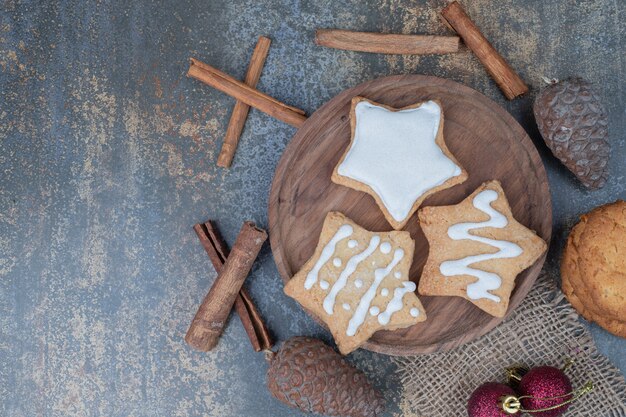 Três estrelas de biscoitos de Natal doce na placa de madeira com bolas vermelhas, pinha e paus de canela.