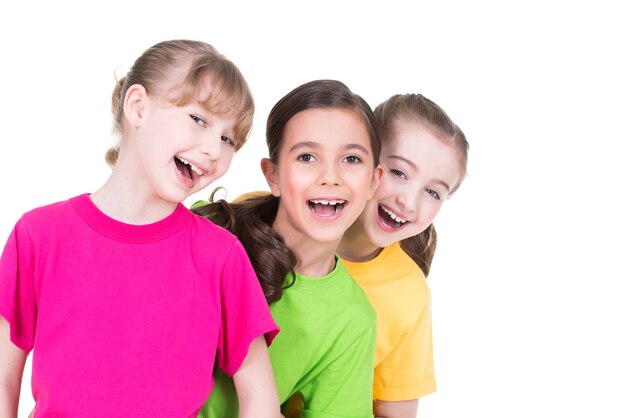 Três fofinhos fofos meninas sorridentes em camisetas coloridas ficam atrás umas das outras no fundo branco.