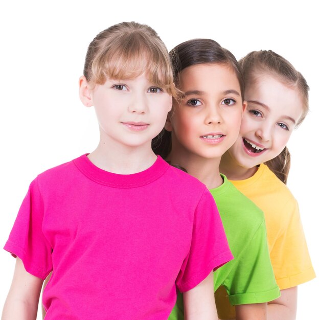 Três fofinhos fofos sorridentes meninas em camisetas coloridas estão atrás uns dos outros na parede branca.