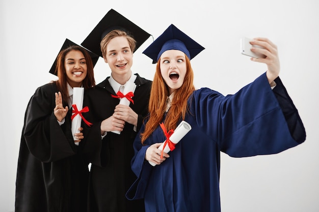 Três graduados felizes alegres brincando se divertindo sorrindo fazendo selfie com diplomas nas mãos, futuros advogados.