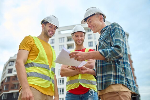 Três homens com desenho discutindo no canteiro de obras