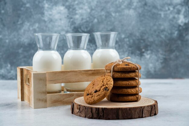 Três jarras de vidro de leite e uma pilha de biscoitos na mesa de mármore.