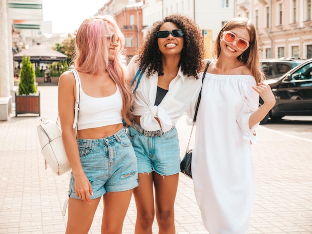 Três jovem linda mulher sorridente em roupas de verão da modaMulheres multirraciais despreocupadas sexy posando no fundo da ruaModelos positivos se divertindo em óculos de sol Alegre e feliz