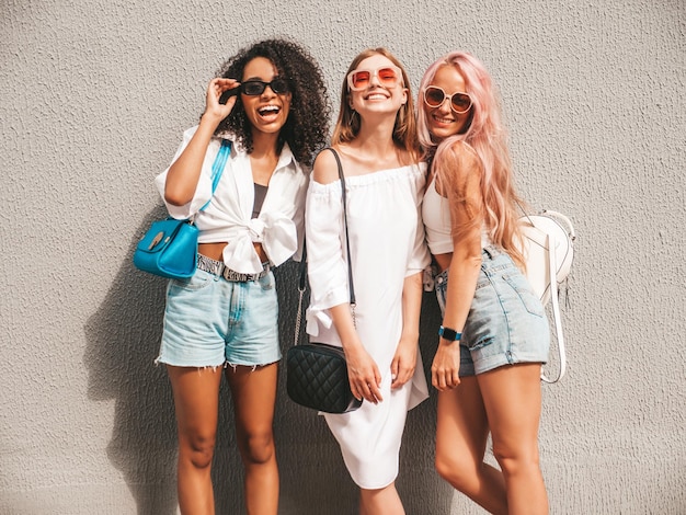 Três jovem linda mulher sorridente em roupas de verão da modaMulheres multirraciais despreocupadas sexy posando no fundo da ruaModelos positivos se divertindo em óculos de sol Alegre e feliz