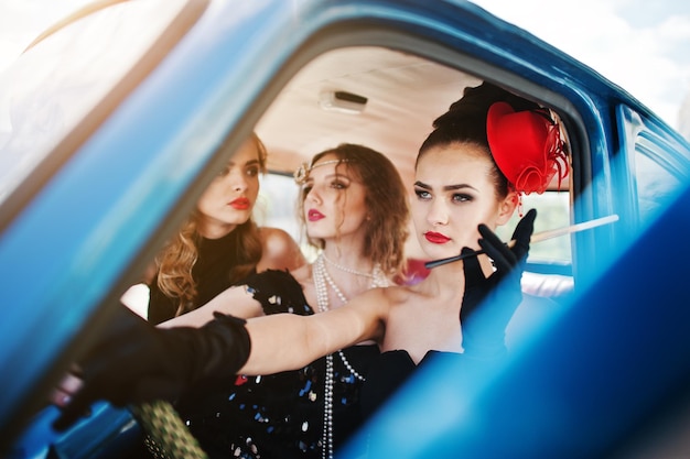 Três jovens em assento de vestido estilo retrô no velho carro clássico vintage