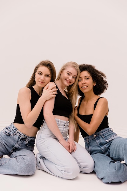 Foto grátis três jovens interraciais morenas loiras e louras em roupas casuais estão sentadas juntas em fundo branco