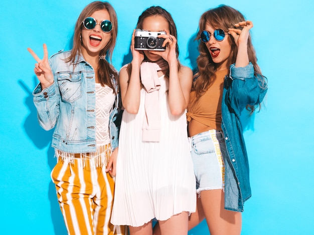 Três jovens lindas meninas sorridentes em vestidos casuais de verão na moda e em óculos de sol. mulheres sexy despreocupadas posando. tirando fotos na câmera retro