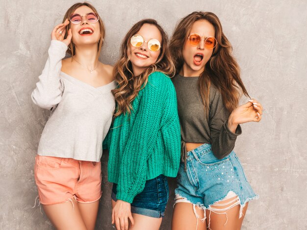 Três jovens lindas sorrindo lindas garotas em roupas da moda no verão. Mulheres sexy despreocupadas posando. Modelos positivos se divertindo em óculos de sol redondos