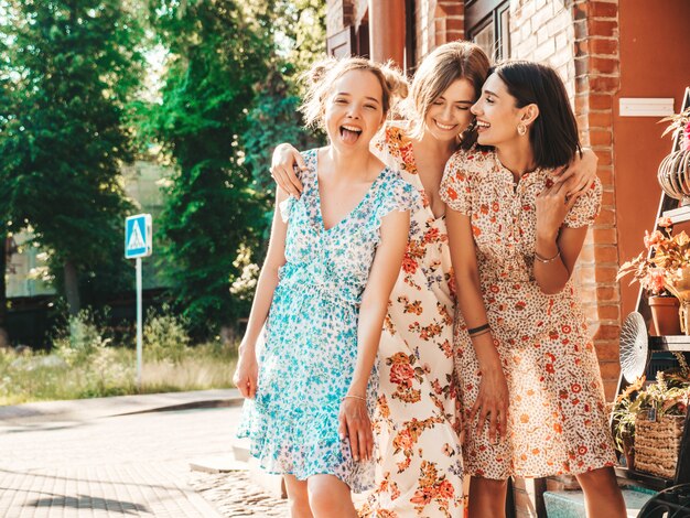 Três lindas meninas sorridentes no vestido de verão na moda posando na rua