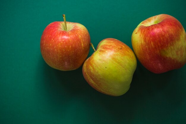 Três maçãs vermelhas inteiras no fundo verde