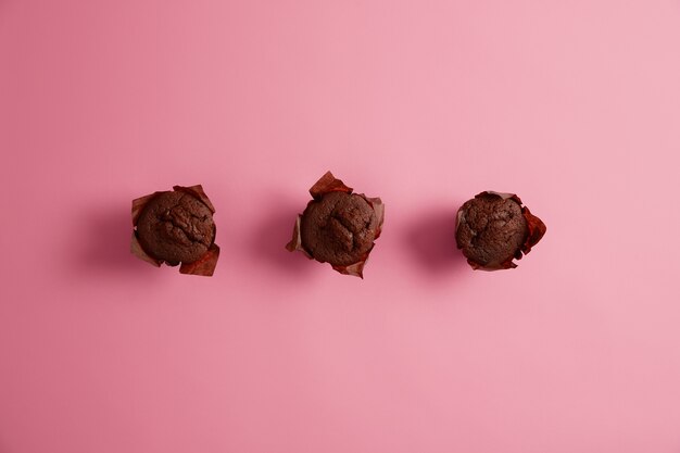 Três muffins de chocolate caseiros para comer com o chá. Bolinhos saborosos comprados na padaria. Bolos para o café da manhã ou piquenique em família. Conceito de padaria e confeitaria. Sobremesa deliciosa e doce.