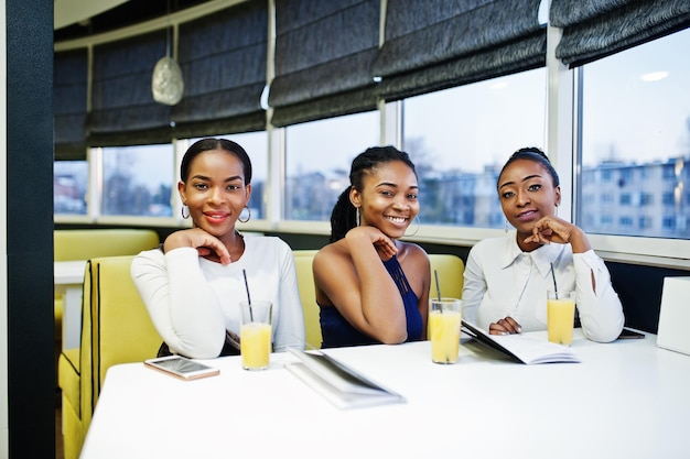 Três mulheres africanas de vestido posando no restaurante leram o menu