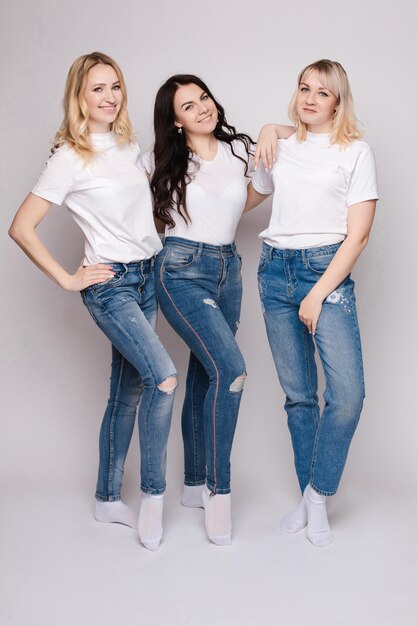 Três mulheres bonitas em camisas brancas e jeans posando