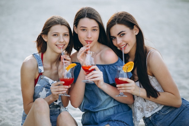 Três mulheres felizes na praia com cocktails