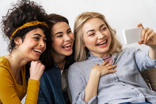 Três mulheres felizes sorrindo e tirando uma selfie