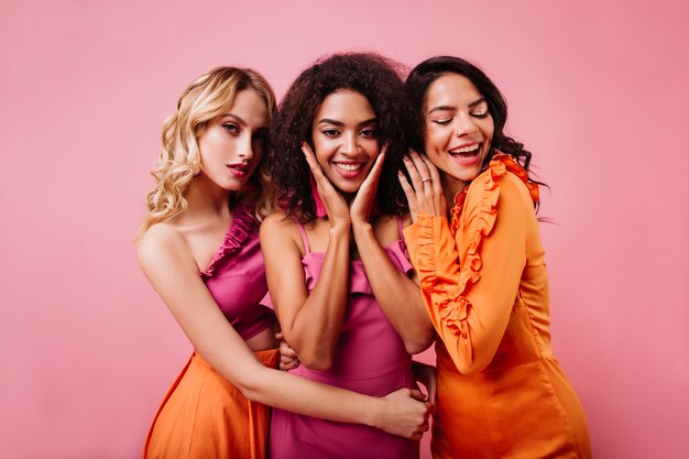 Três mulheres fofas posando juntas na parede rosa