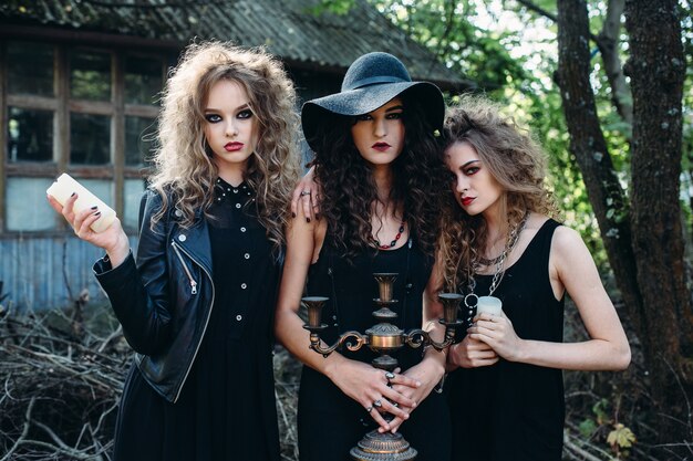 Três mulheres vintage como bruxas, posam em frente a um prédio abandonado na véspera do Halloween