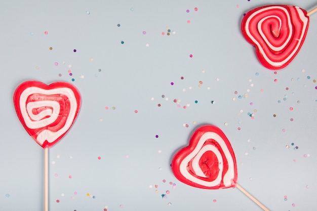 Foto grátis três pirulitos vermelhos da forma do coração no fundo cinzento com confetes coloridos