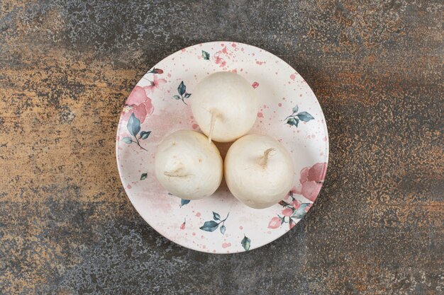 Três rabanetes no prato, na superfície do mármore