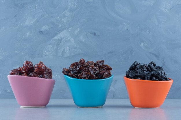 Três tigelas de frutas secas, na mesa de mármore.
