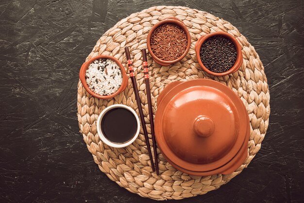 Três tigelas de grãos de arroz cru com molho de soja; pauzinhos no placemat