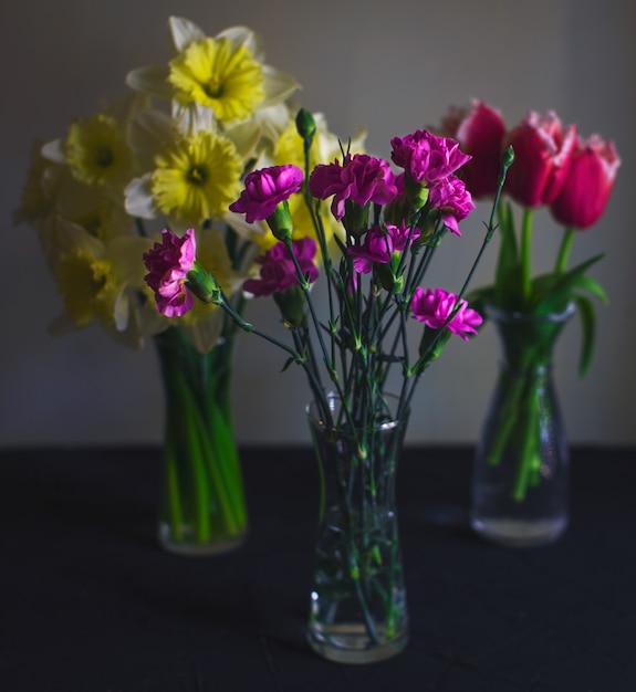 Três vasos de vidro de cravo, narciso, tulipas