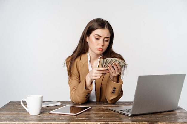 Foto grátis triste empresária contando dinheiro no escritório com cara decepcionada chateada baixa renda posando contra quem...