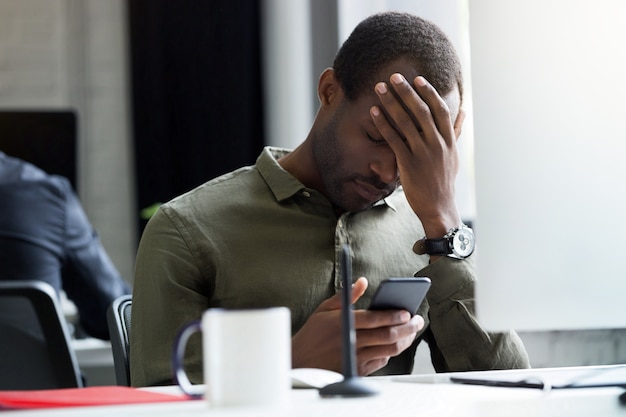 Foto grátis triste jovem africano lendo a mensagem em seu telefone móvel