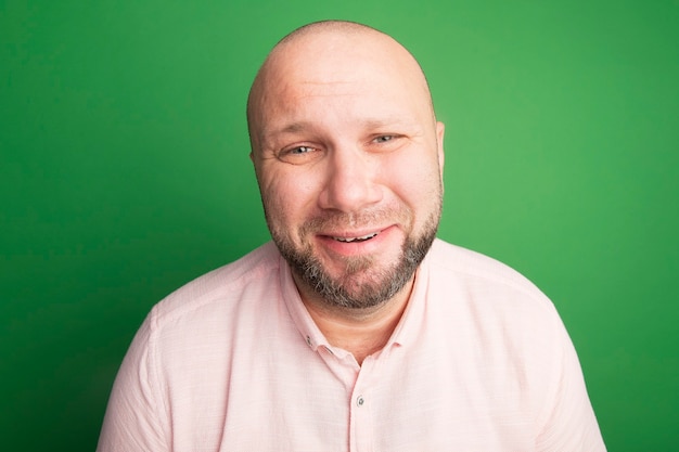 Triste olhando para a frente, homem careca de meia-idade vestindo camiseta rosa isolada no verde