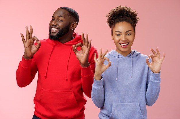 Tudo perfeito. Encantador relacionamento amoroso de dois casais namorada afro-americana namorado mostrando ok ok excelente gesto sorrindo em aprovação assegure aos pais que eles estão bem, fundo rosa