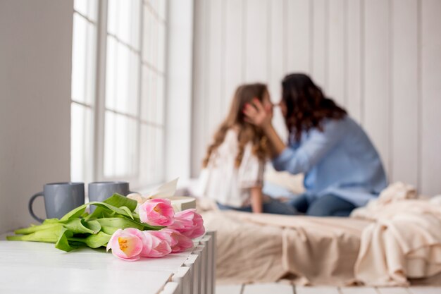 Tulipa flores na mesa perto da cama com abraçar mãe e filha