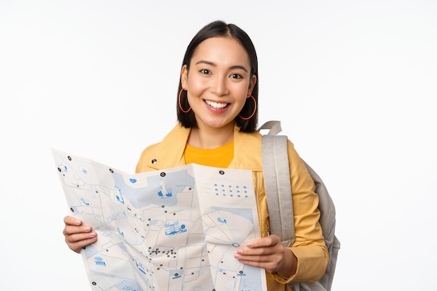 Turismo e mochila Sorrindo menina asiática segurando mapa e mochila turista procurando caminho viajando em pé sobre fundo branco