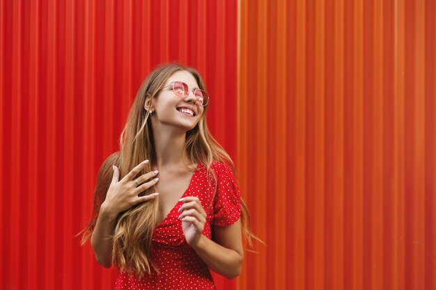 Turismo Mulher feliz comendo sorvete doce ao ar livre e olhando bem sorrindo alegre em pé perto da parede vermelha Viajante feminina explorando a cidade de férias