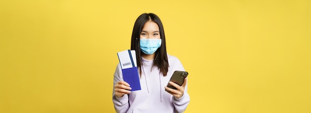 Foto grátis turista asiática com máscara facial segurando telefone celular mostrando passaporte e reserva de passagens aéreas