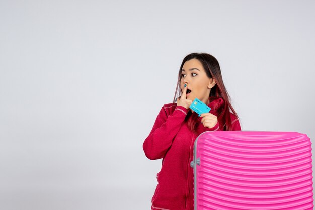 Turista de frente com uma bolsa rosa segurando o cartão do banco na parede branca