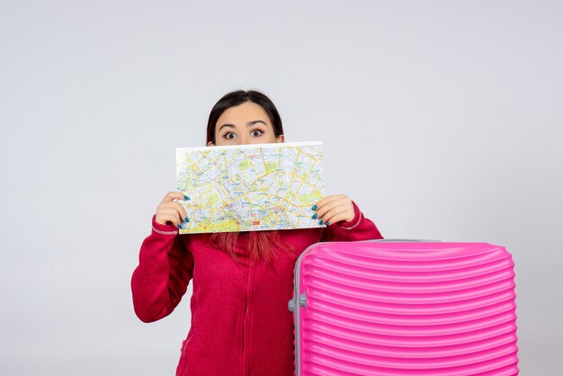 Turista de frente com uma bolsa rosa segurando o mapa na parede branca