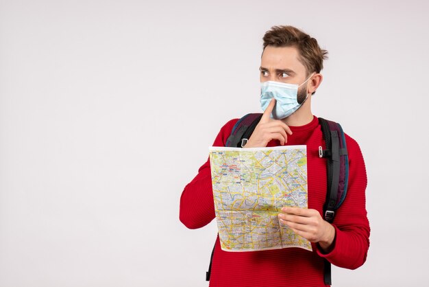 Turista masculino com máscara estéril segurando o mapa na parede branca