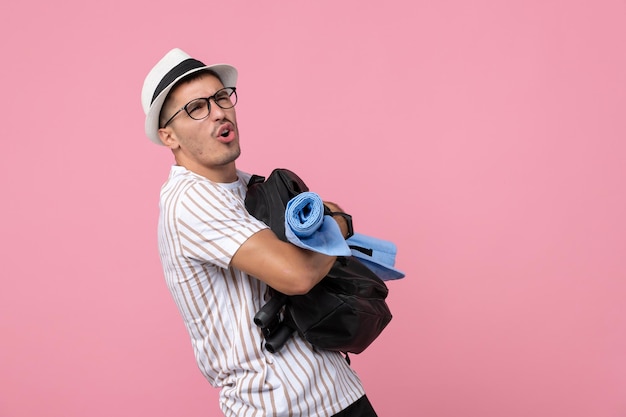 Turista masculino segurando sua mochila na parede cor de rosa turista