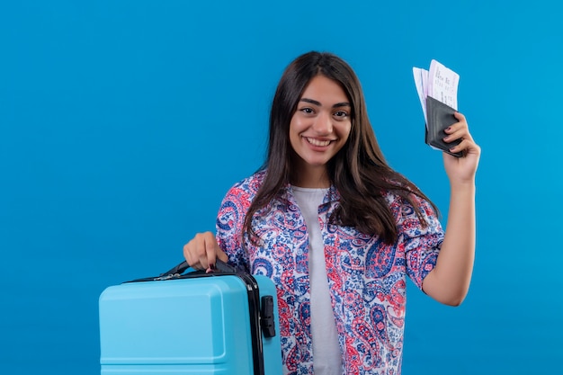 turista mulher segurando uma mala de viagem e passaporte com bilhetes com um sorriso no rosto feliz e positivo
