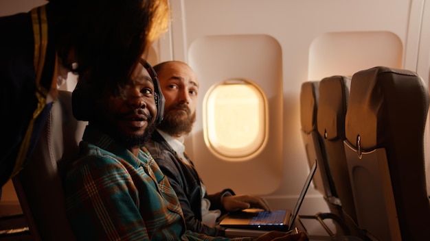 Turista usando telefone celular e voando em jato de avião para sair de férias, esperando para chegar ao destino. Viajando em classe econômica em voo durante o pôr do sol, navegando no smartphone.