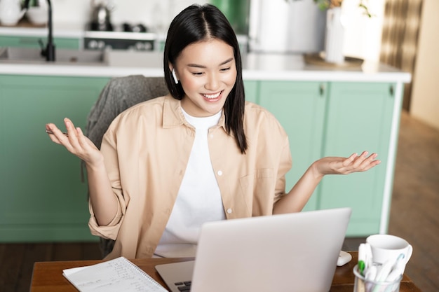 Tutora asiática tendo aulas on-line em casa, trabalhando em um laptop, tendo videoconferência e ...