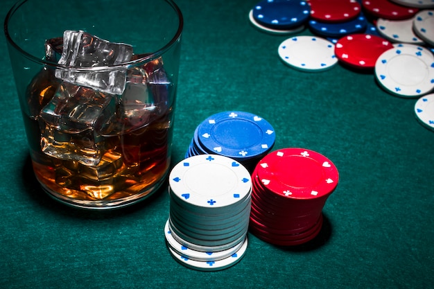 Uísque com cubos de gelo e fichas de casino pilha no pano de fundo verde poker