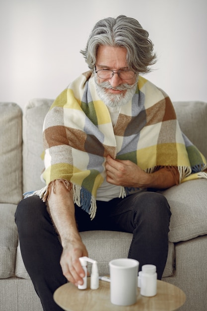 Foto grátis Último homem sozinho sentado no sofá. homem doente coberto com manta. grangfather com uma xícara de chá.