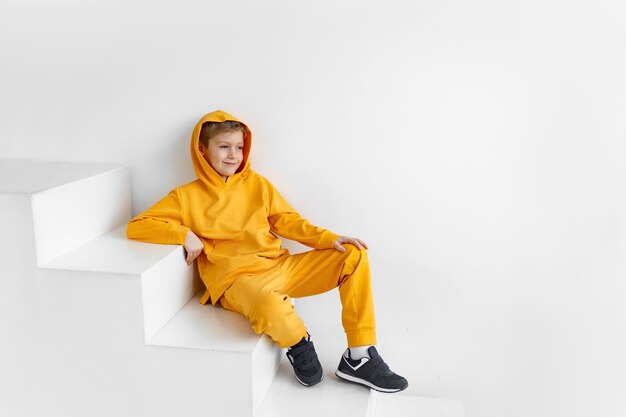Um adolescente em um agasalho amarelo em um fundo monocromático em um capuz está sentado nos degraus