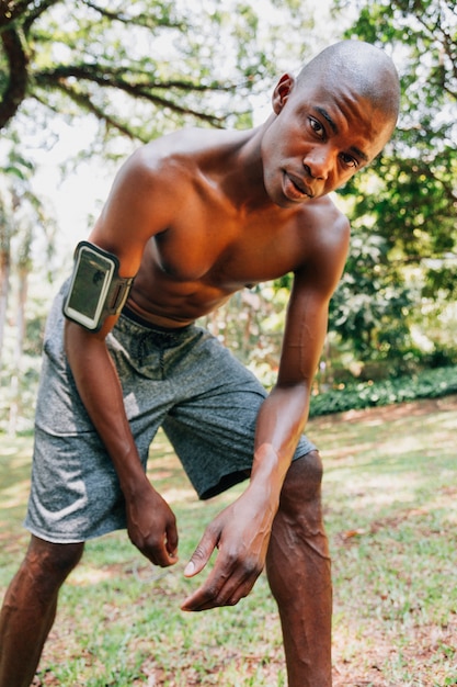 Um, africano, ajuste, homem jovem, com, braçadeira, seu, mão, olhando câmera, em, a, parque