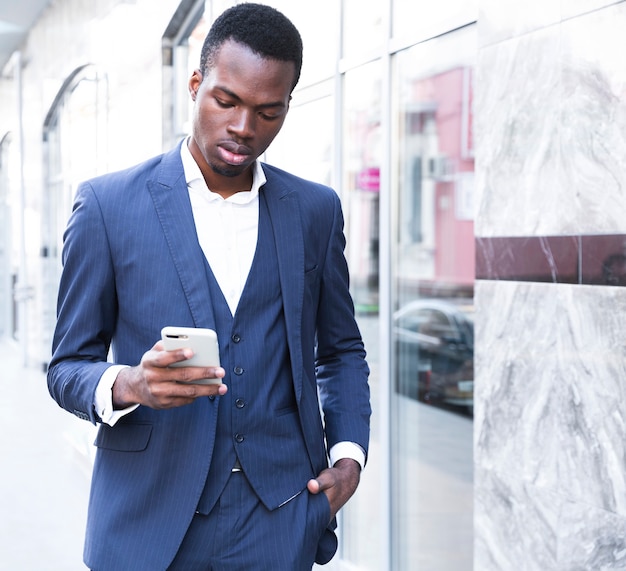 Um, africano, jovem, homem negócios, com, seu, mãos, em, seu, bolso, usando, telefone móvel