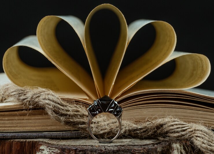 Foto grátis um anel com pedras cor de vinho na frente do livro aberto, estilo rústico