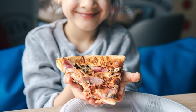 Um apetitoso pedaço de pizza nas mãos de uma garotinha