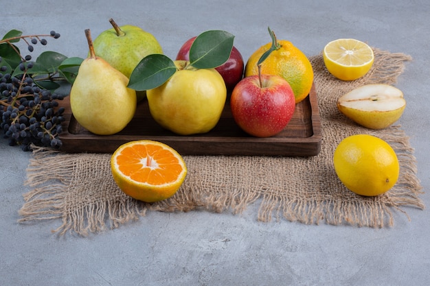 Um arranjo de várias frutas em uma placa de madeira e um pedaço de pano no fundo de mármore.