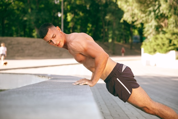 Um atleta masculino musculoso fazendo exercícios no parque. Ginástica, treino, flexibilidade de treino de fitness. Cidade de verão em dia ensolarado Estilo de vida ativo e saudável, juventude, musculação.